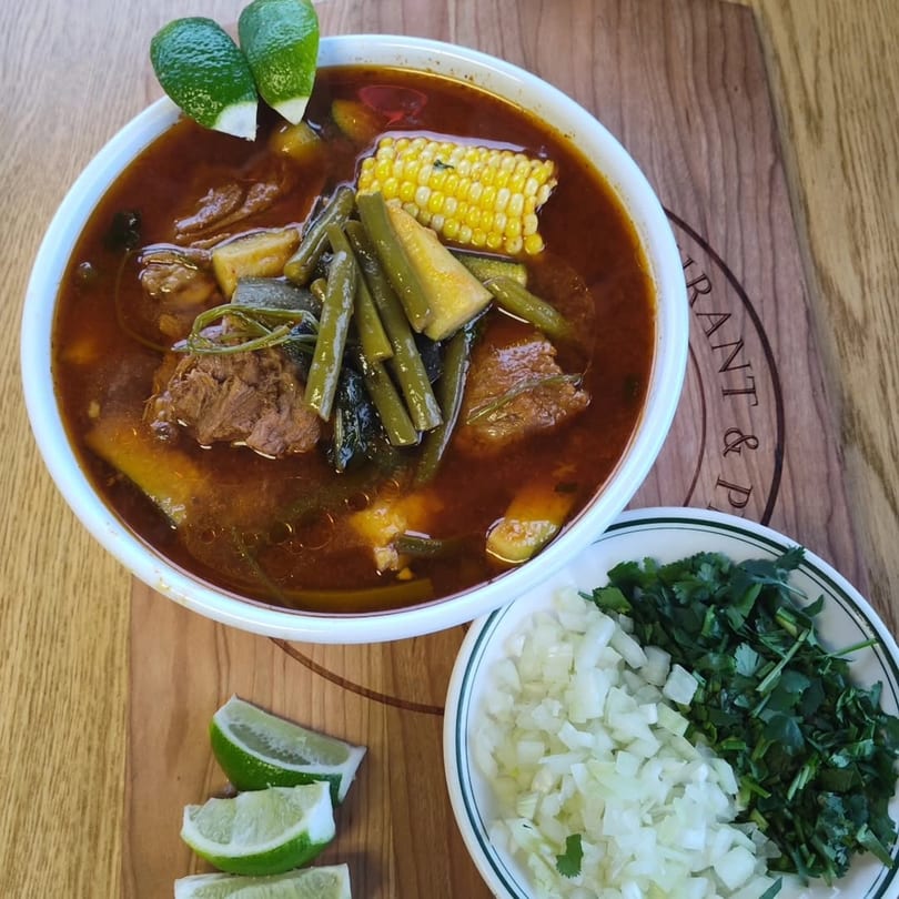 Hearty beef and vegetable soup with corn, green beans, and lime, served with chopped onions and cilantro.