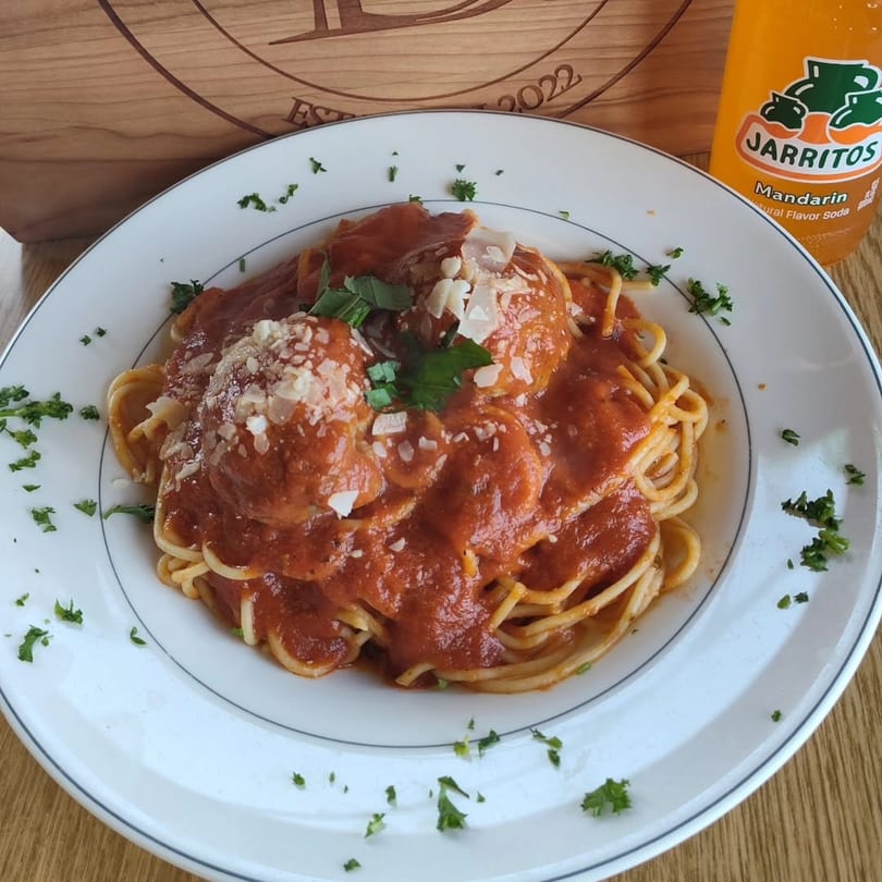 Spaghetti and meatballs with red sauce, parmesan, and parsley, next to a Jarritos soda.