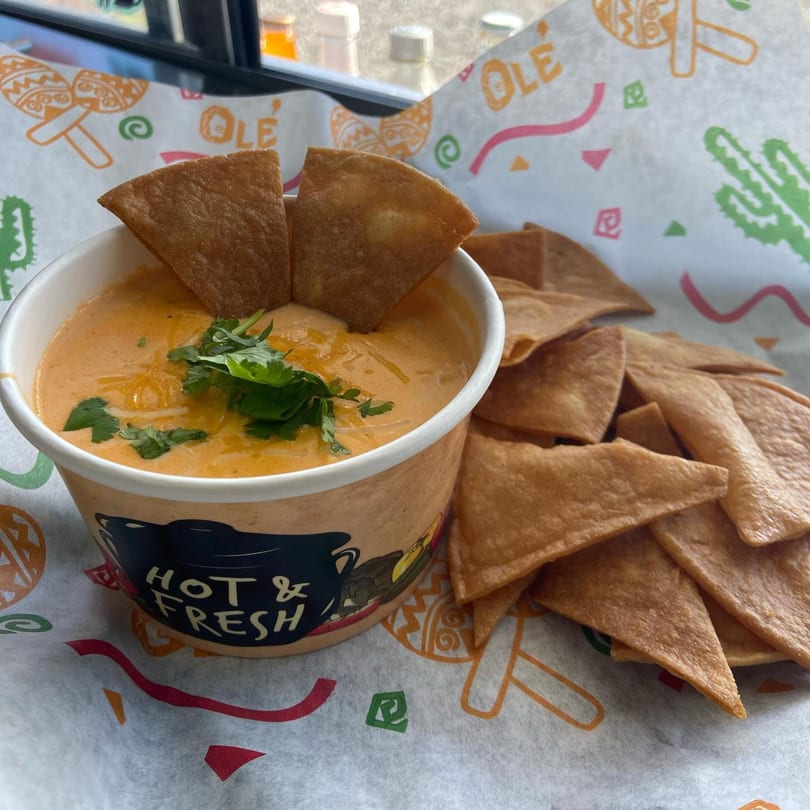 Queso dip with cilantro and tortilla chips on branded paper from Delicias Sobre Ruedas.