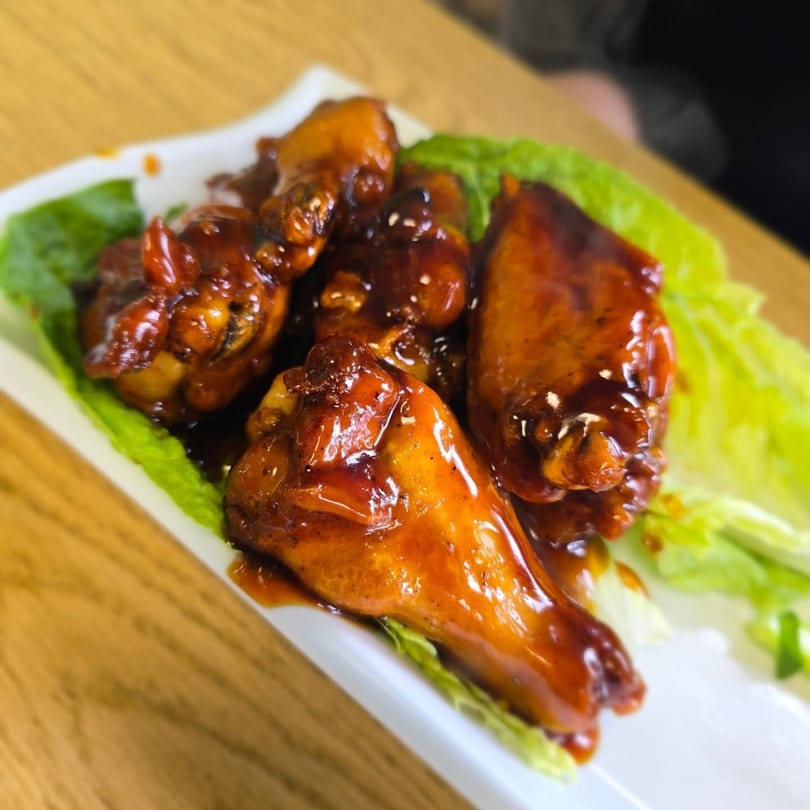 Sweet and spicy chicken wings on a bed of lettuce, served on a white rectangular plate.